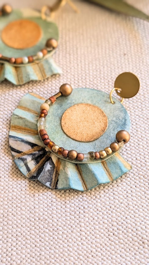 Textured view of pleated edge and beaded arc on sculptural watercolour paper earring with earthy gold and black tones.