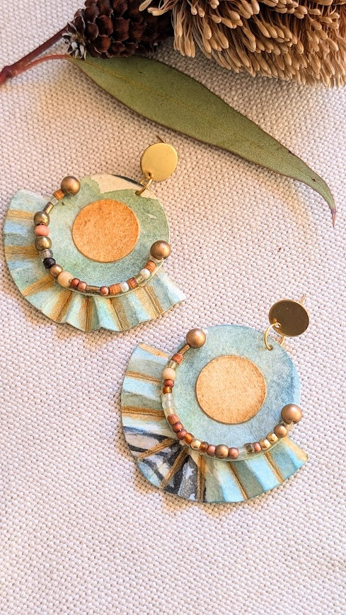 Bold sculptural earrings made from watercolour paper and brass, shown from an angled top-down view on natural fabric