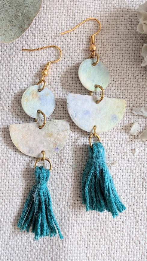 Earrings with half-circle shapes and blue tassels on a textured surface