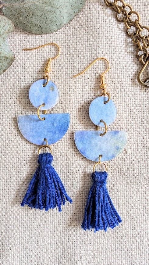 Blue tassel earrings with gold accents on a textured surface