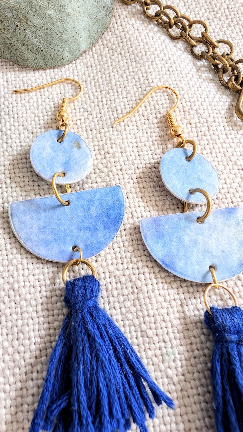 Blue tassel earrings with gold hooks on a textured surface