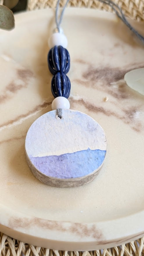 Round pendant with blue and purple coloration on a textured surface