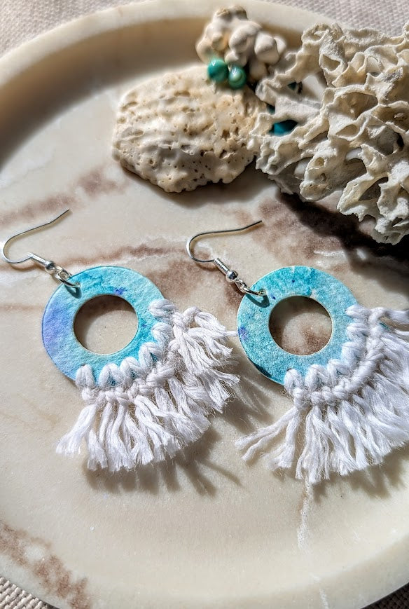 Pair of earrings with turquoise circular design and white fringe on a stone surface.