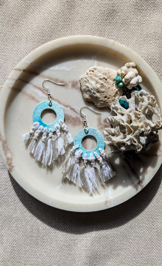Pair of earrings with turquoise and white design on a stone surface with coral.