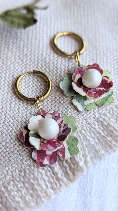 Close-up of a pair of handmade floral earrings from the Elowen Collection by Paper & Palette Studio. Each earring features layered watercolour paper petals in deep burgundy, soft green, and ivory, with a central faux pearl, hanging from gold huggie hoops. Displayed on a cream textured fabric with a soft, natural backdrop.