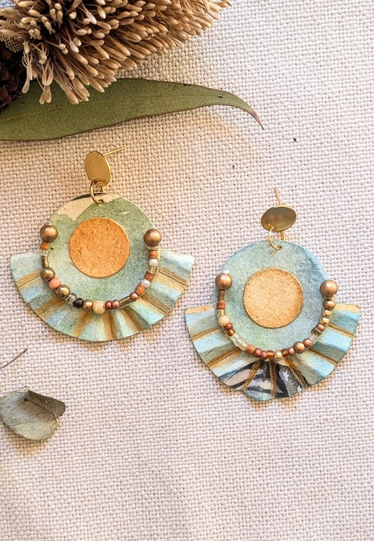 “Pair of handcrafted fan earrings with painted circular centre, beaded curve, and paper pleats in aqua and ochre tones.”