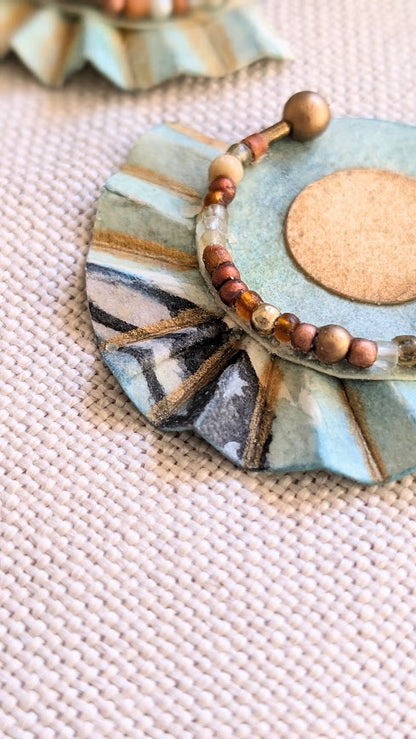 Macro detail of pleated paper earring showing metallic brushstrokes and mixed gold-toned beads in a semi-circle arrangement.