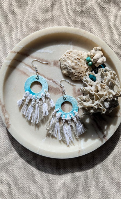 Pair of earrings with turquoise and white design on a stone surface with coral.