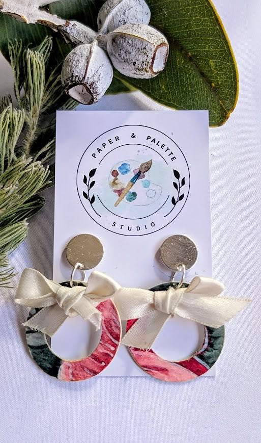 Earrings with floral design and bows on a 'Paper & Palette Studio' card, surrounded by greenery.