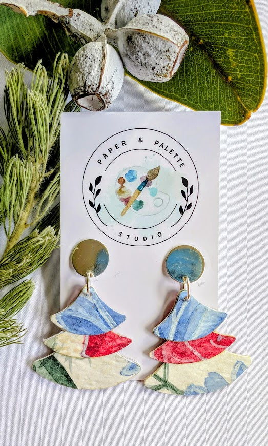 Colorful layered earrings on a 'Paper & Palette Studio' card with greenery around.