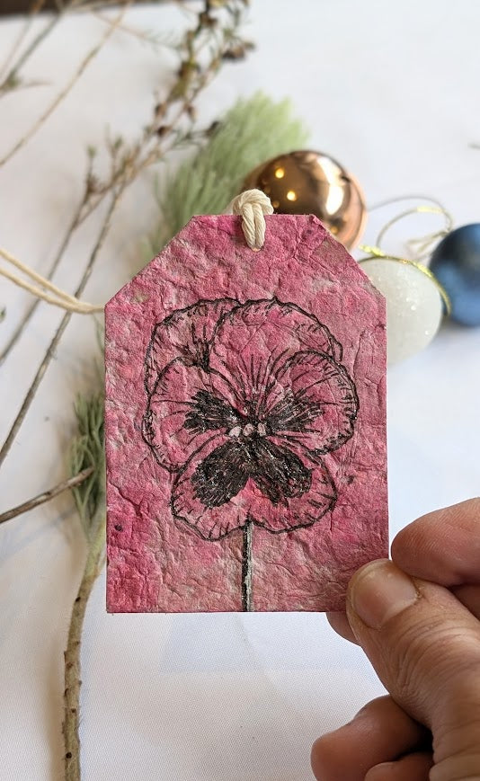 Pink floral tag held by a hand with natural elements in the background