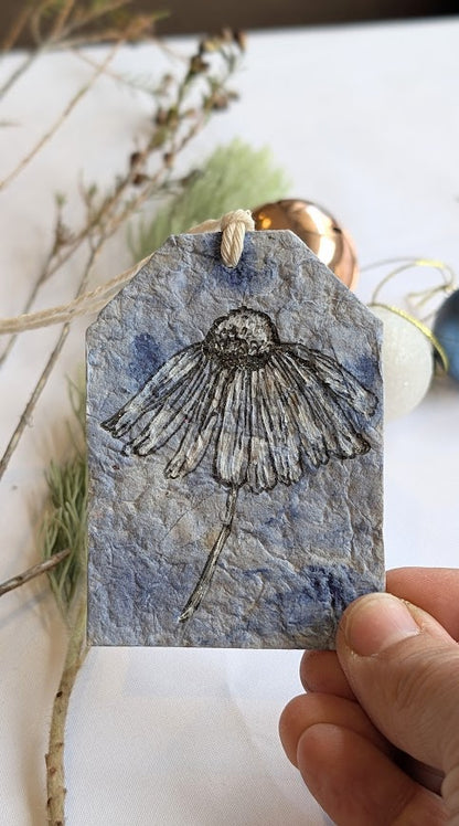 Handmade paper tag with a floral design held by a hand on a white background