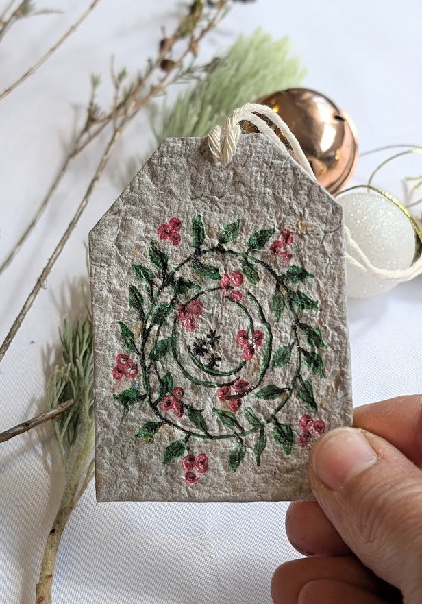 Handmade tag with floral decoration held by a hand, with natural elements in the background.